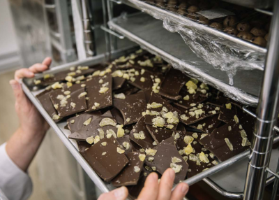 A person holds a tray of chocolate bark in an industrial kitchen
