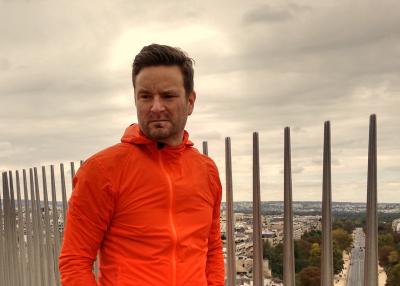 Richard leBrasseur, a short-haired man wearing an orange jacket, stands outdoors overlooking a city